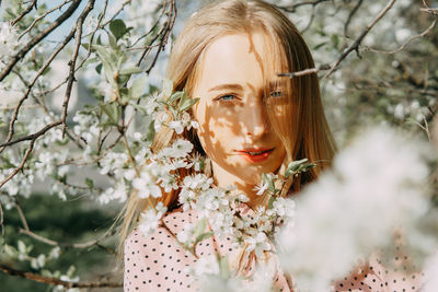 Blonde girl on a spring walk in the garden with cherry blossoms. female portrait, close-up. 