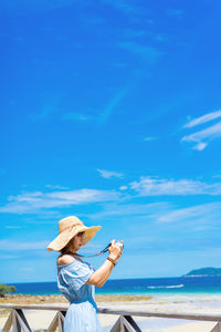 Side view of woman photographing at beach against blue sky