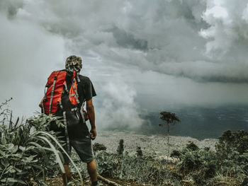 Rear view of hiker standing while looking at cloudy sky