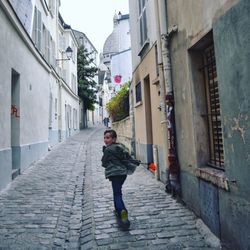 Full length of boy running on cobbled alley amidst buildings in town