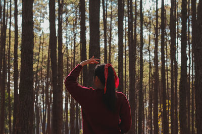 Rear view of woman standing by trees in forest