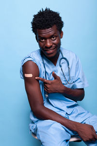 Young man sitting against blue background