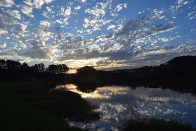 Reflection of silhouette trees in calm lake at sunset