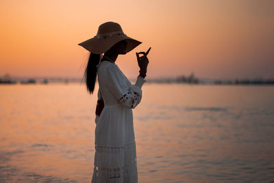 Beautiful african woman in sun hat walks on beach at sunset. calming coral  trendy in color of 2022.