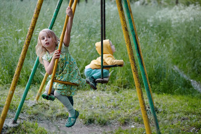 Siblings swinging against plants in park