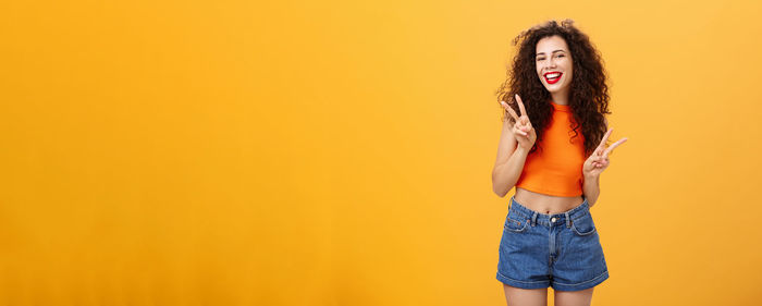 Young woman standing against yellow background