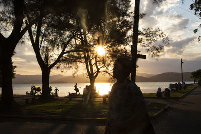 Silhouette people standing by trees against sky during sunset