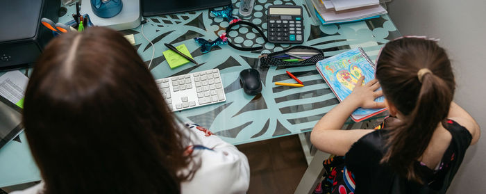 High angle view of mother and daughter sitting at desk