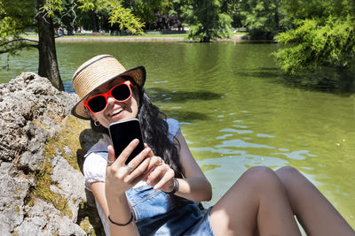 Midsection of woman sitting on rock by lake