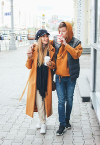 Smiling young couple holding disposable cups while walking in city