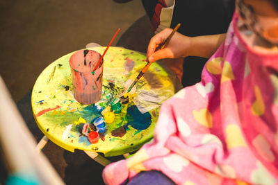 An little artist is dipping a paint brush into a watercolor palette.