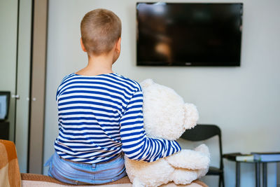 Cute boy and his plush toy bear are watching tv while sitting on the couch