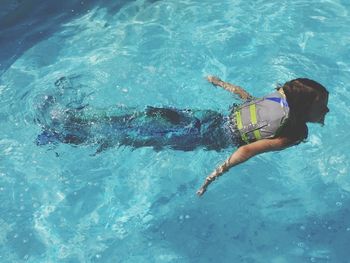 High angle view of girl wearing life jacket while swimming in pool during sunny day