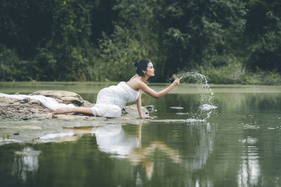 Woman splashing water in lake against trees