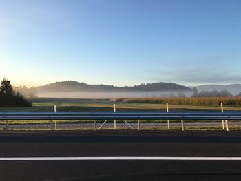 Road by railing against clear sky