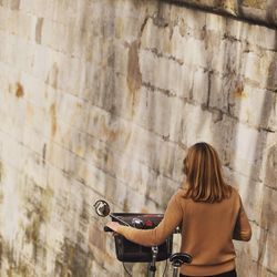 Rear view of woman with bicycle by wall