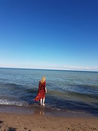 Woman with umbrella on beach against clear blue sky