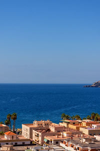 High angle view of townscape by sea against clear blue sky