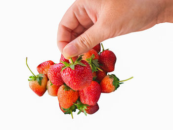 Close-up of hand holding strawberry over white background