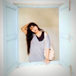 Portrait of young woman standing by window at home