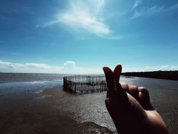 Person hand by sea against sky