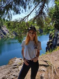 Portrait of beautiful young woman standing on rock against trees