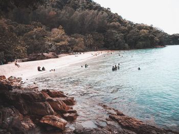 Group of people on rock by sea against sky