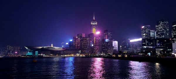 Illuminated buildings by river against sky at night