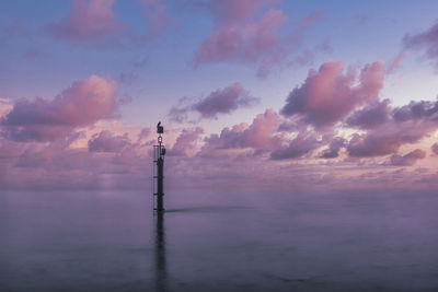 Silhouette tower by sea against sky during sunset