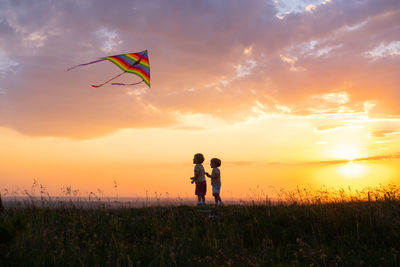 Rear view of woman standing on field against sky during sunset