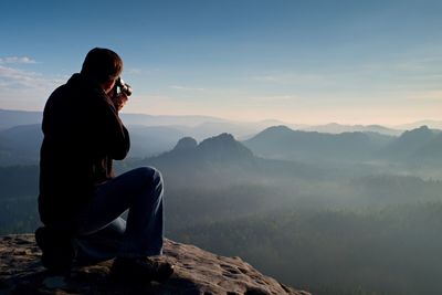 Man sitting on mountain against sky during sunset