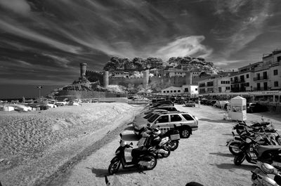 Vehicles parked at beach in town against cloudy sky