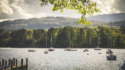 Sailboats sailing in river by mountains against sky