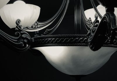 Low angle view of illuminated electric lamp hanging against black background