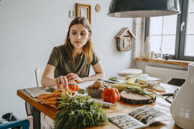 Young female entrepreneur holding carrots sitting at table in studio