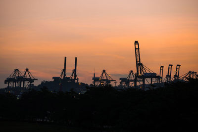 Silhouette cranes on pier against sky during sunset