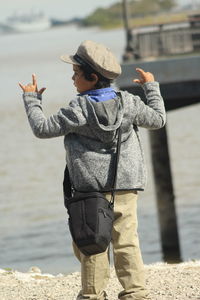 Rear view of boy gesturing while standing at beach