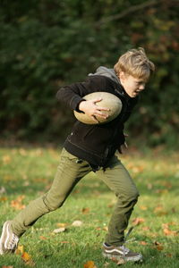 Full length of boy holding rugby ball while running on land