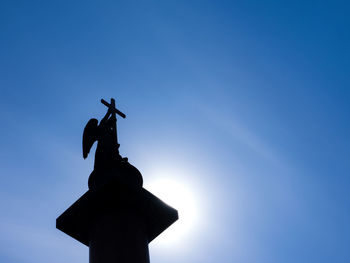 Low angle view of silhouette statue against blue sky