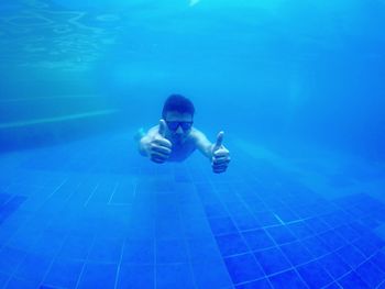 Portrait of man gesturing thumbs up while underwater in swimming pool