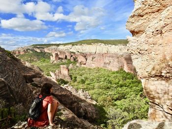 Rear view of man standing on cliff against cloudy sky