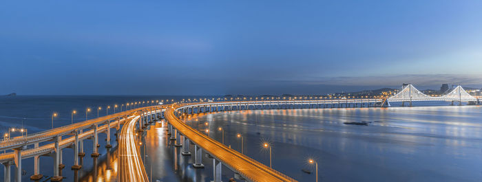 Illuminated bridge over sea against sky at night