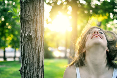 Cheerful young woman by tree at park on sunny day