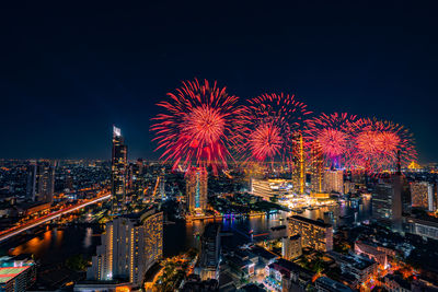 Red firework display over city lit up at night. high angle view of illuminated buildings 