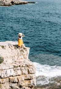 Young woman in summer outfit standing on cliffs above sea.