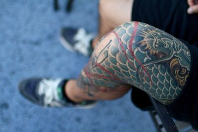 Low section of tattooed man sitting on railing