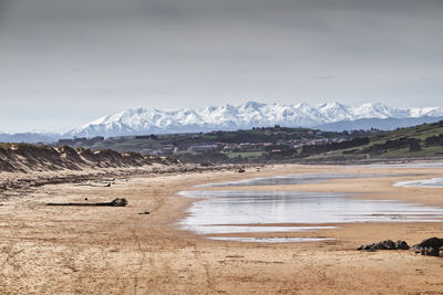 Scenic view of beach and snowcapped mountains against sky