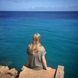 Rear view of young woman sitting at sea shore against sky