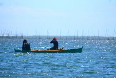 People rowing boat in sea against sky