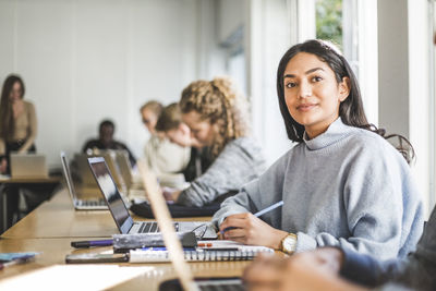 Portrait of confident young woman at desk in classroom